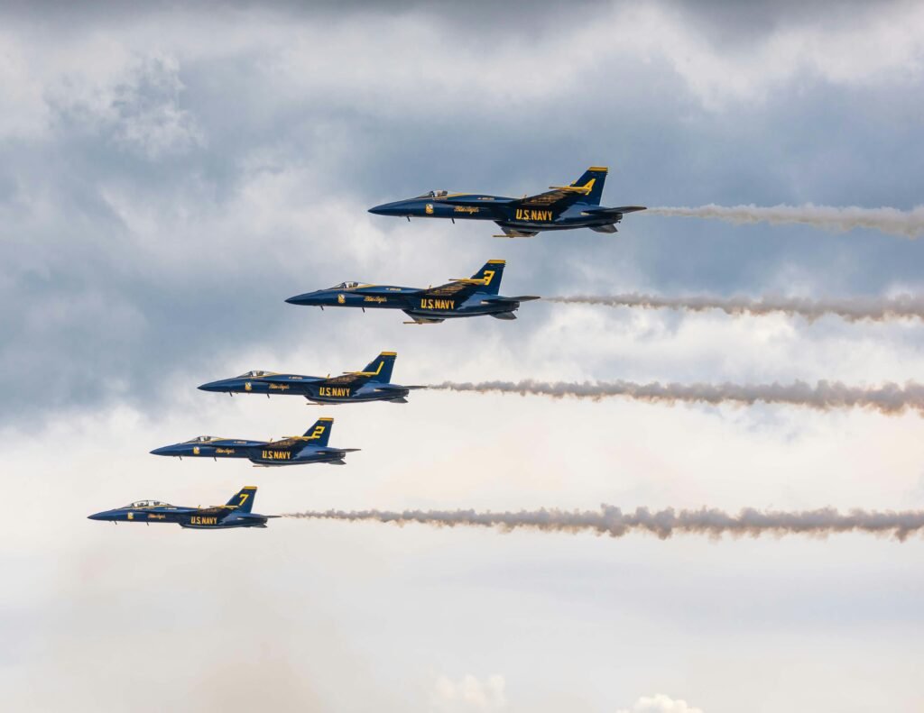 Five U.S. Navy Blue Angels jets flying in tight formation against a cloudy sky.